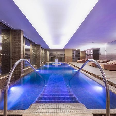 Ap Lago Montargil - Conference & Spa Luaran gambar The photo shows a modern indoor swimming pool area. The pool features a sleek design with steps leading into the water and a gentle curve at the sides. The water is illuminated in a blue hue, enhancing the relaxing atmosphere. Surrounding the pool ar