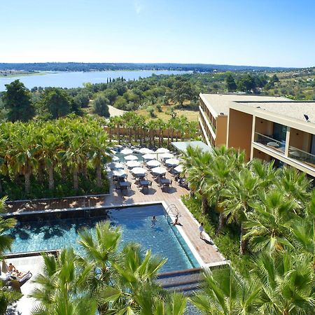 Ap Lago Montargil - Conference & Spa Luaran gambar The photo shows a scenic view of a modern hotel or resort. In the foreground, there is a swimming pool surrounded by palm trees, with lounge chairs positioned beside it. Sun umbrellas provide shade over the chairs. The background features a lush land