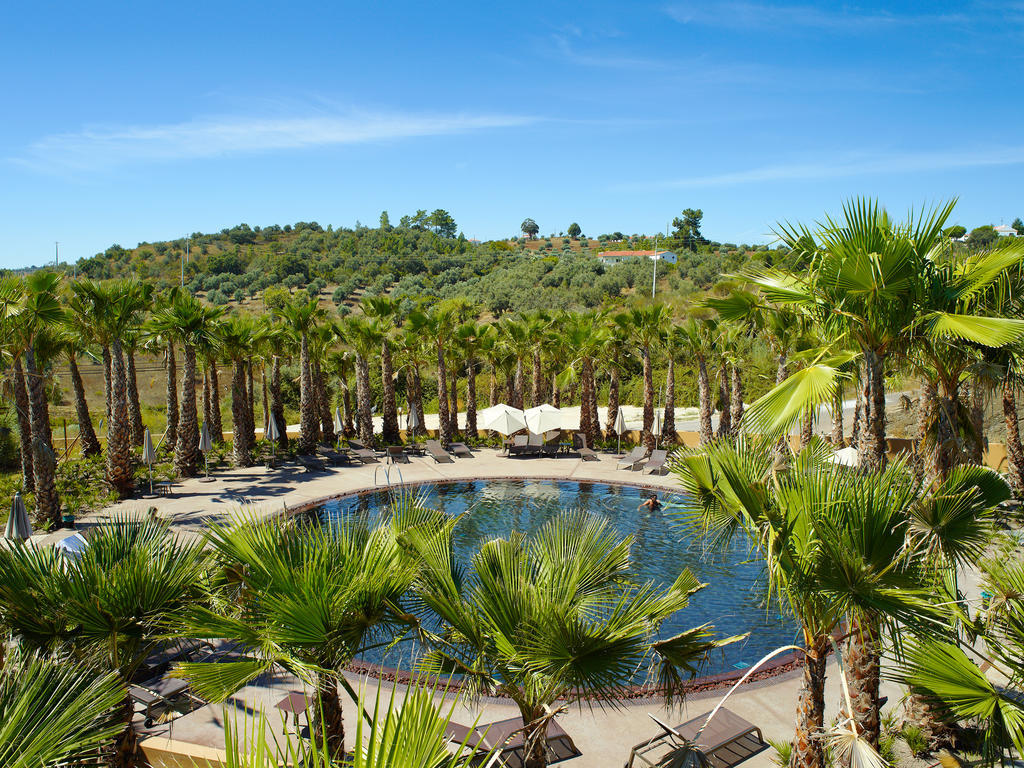 Ap Lago Montargil - Conference & Spa Luaran gambar The photo depicts a beautiful outdoor area featuring a circular swimming pool surrounded by palm trees. The pool area has several lounge chairs arranged around it. In the background, there is a lush green hillside, and the sky is clear with a bright 