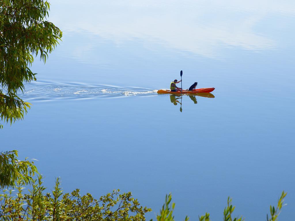 Ap Lago Montargil - Conference & Spa Luaran gambar The photo shows a serene scene of a person kayaking on a calm body of water. The surface of the water is very smooth, reflecting the surroundings, and there is a gentle wake behind the kayak indicating movement. The kayaker is wearing a life jacket a