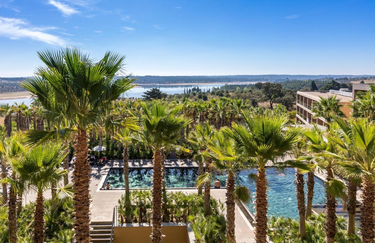 Ap Lago Montargil - Conference & Spa Luaran gambar The photo depicts a picturesque resort landscape with a clear blue sky. In the foreground, there are tall palm trees surrounding a swimming pool area. The swimming pool has a modern design and is surrounded by lush greenery. In the background, you ca