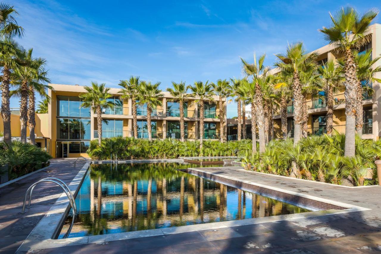 Ap Lago Montargil - Conference & Spa Luaran gambar The photo features a modern building surrounded by lush greenery and palm trees. In the foreground, there is a serene swimming pool with a reflective surface that captures the surrounding environment. The architecture of the building appears to have 