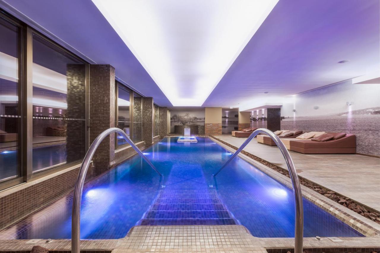 Ap Lago Montargil - Conference & Spa Luaran gambar The photo shows a modern indoor swimming pool area. The pool features a sleek design with steps leading into the water and a gentle curve at the sides. The water is illuminated in a blue hue, enhancing the relaxing atmosphere. Surrounding the pool ar