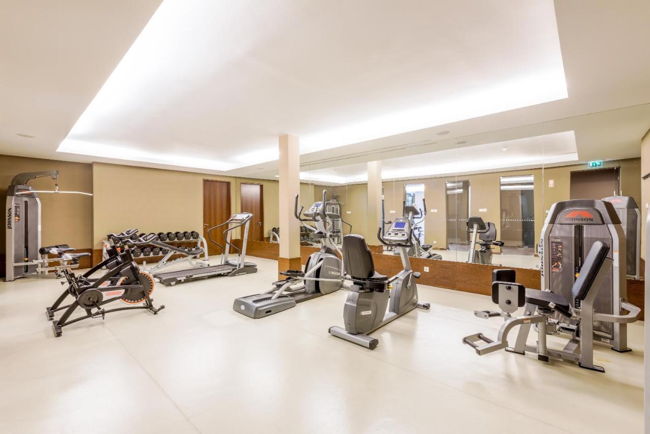 Ap Lago Montargil - Conference & Spa Luaran gambar The image shows a modern gym interior featuring various exercise equipment. On the left, there are free weights and weight benches. In the center, there are multiple machines, including a stationary bike and an elliptical. The space is well-lit with 