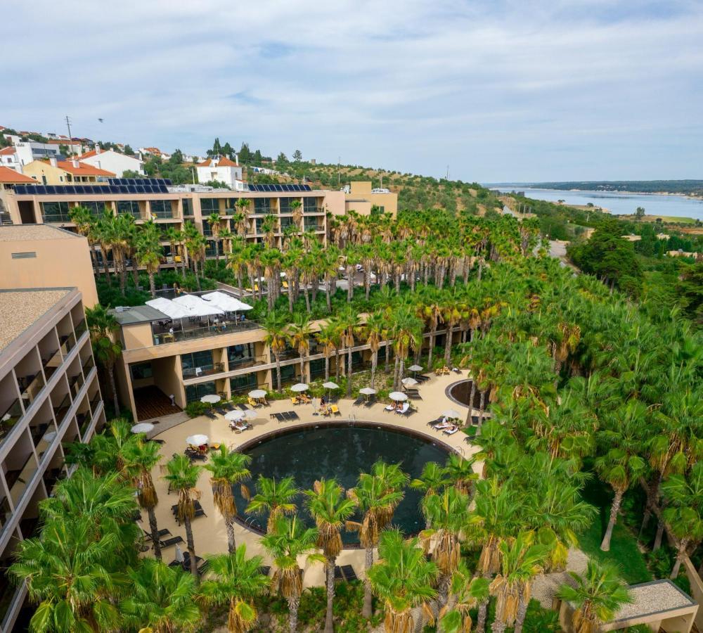 Ap Lago Montargil - Conference & Spa Luaran gambar The photo shows a modern hotel complex set amidst lush greenery, featuring numerous palm trees. In the foreground, there is a circular swimming pool surrounded by lounge chairs. The hotel itself has multiple levels with balconies overlooking the pool