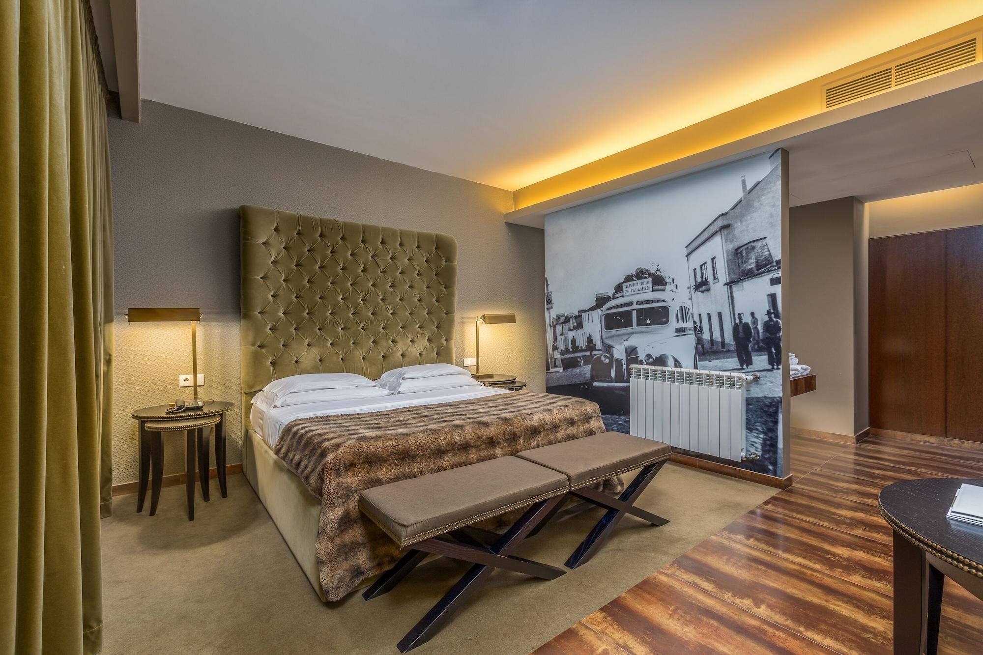 Ap Lago Montargil - Conference & Spa Luaran gambar The photo shows a modern hotel room featuring a king-sized bed with a tufted headboard, dressed in white linens and a decorative throw blanket. On either side of the bed, there are bedside tables with lamps. The room is well-lit, with an ambient ceil