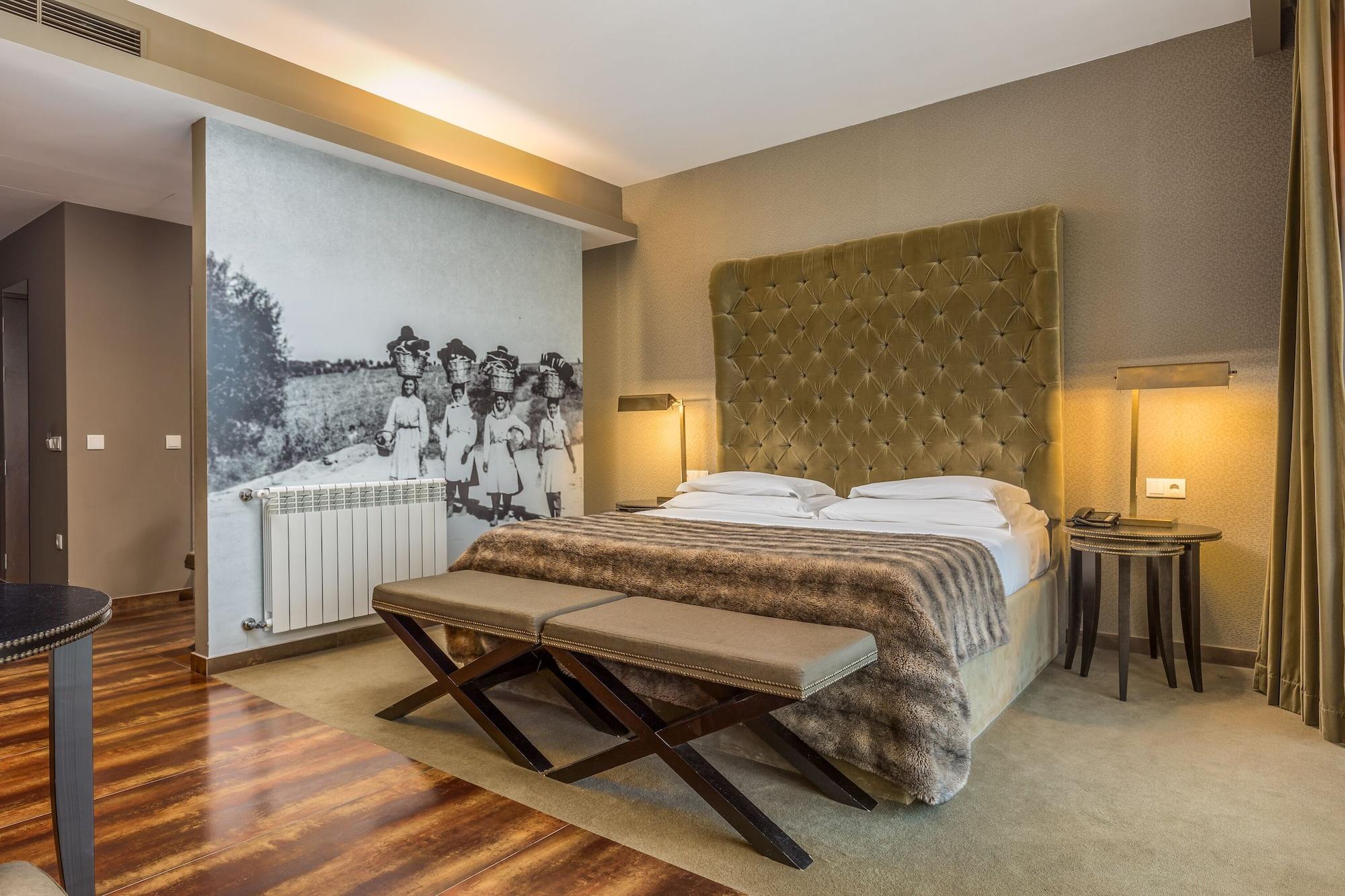 Ap Lago Montargil - Conference & Spa Luaran gambar The photo shows a modern hotel room with a large, plush bed that has a tufted, green headboard. The bedding is white with a textured blanket at the foot of the bed. A decorative wall behind the bed features a black and white mural of children in a fi