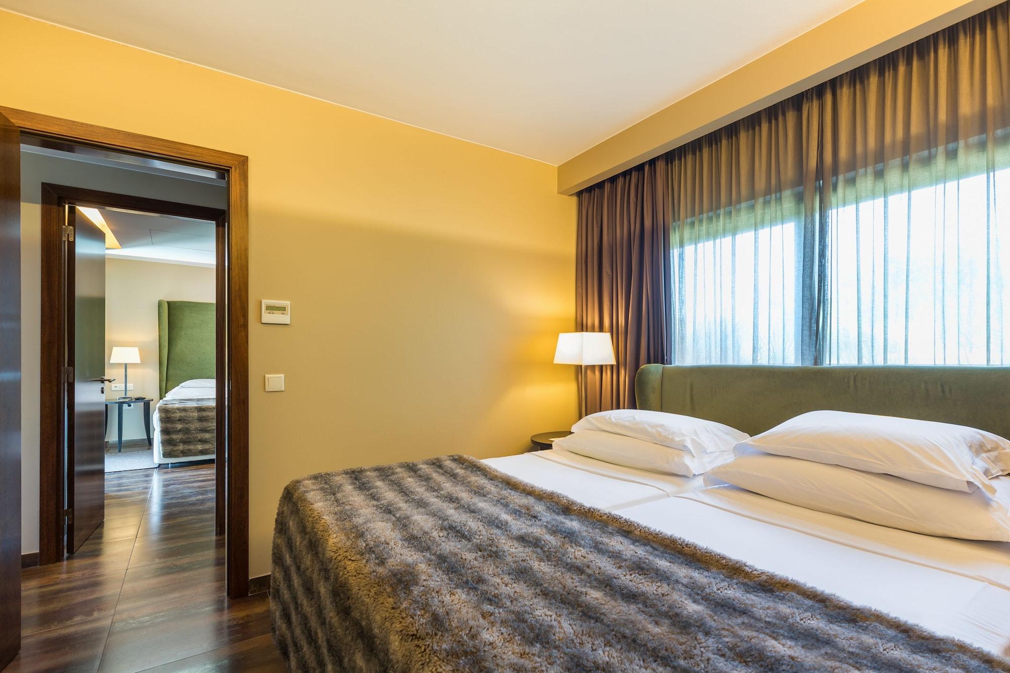 Ap Lago Montargil - Conference & Spa Luaran gambar The photo shows the interior of a well-furnished hotel room. It features two beds with white linens and a gray decorative throw on top. The walls are painted a warm yellow, and there are floor-to-ceiling windows covered with dark curtains that allow 