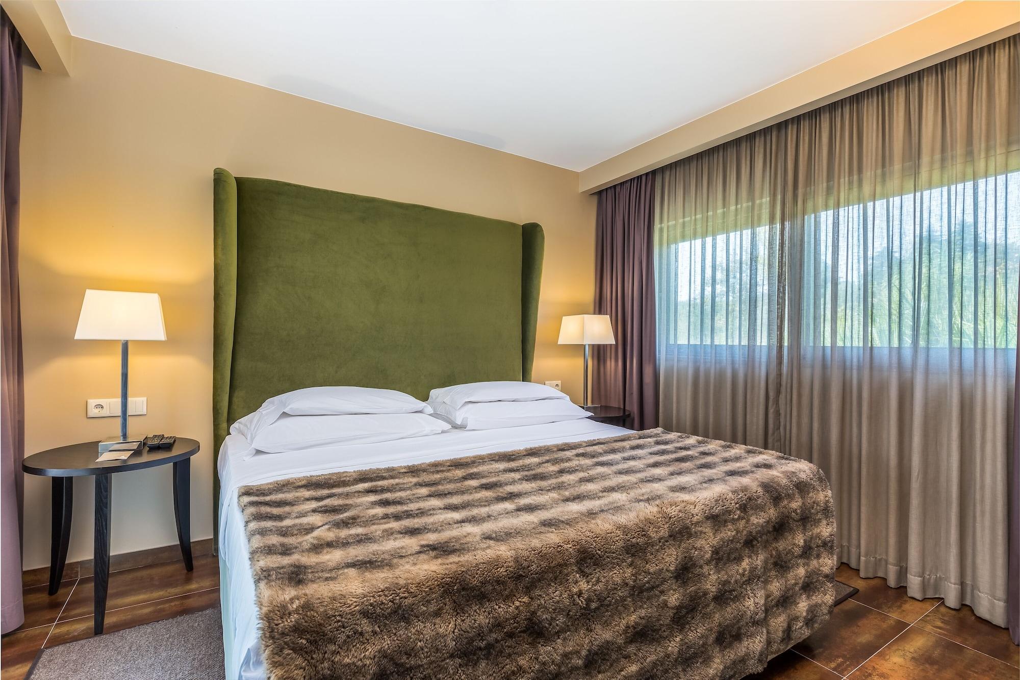 Ap Lago Montargil - Conference & Spa Luaran gambar The photo shows a cozy hotel room featuring a large bed with two white pillows and a fur-style blanket draped over it. Behind the bed is a tall, green headboard that adds a touch of color to the room. On either side of the bed are bedside tables, eac