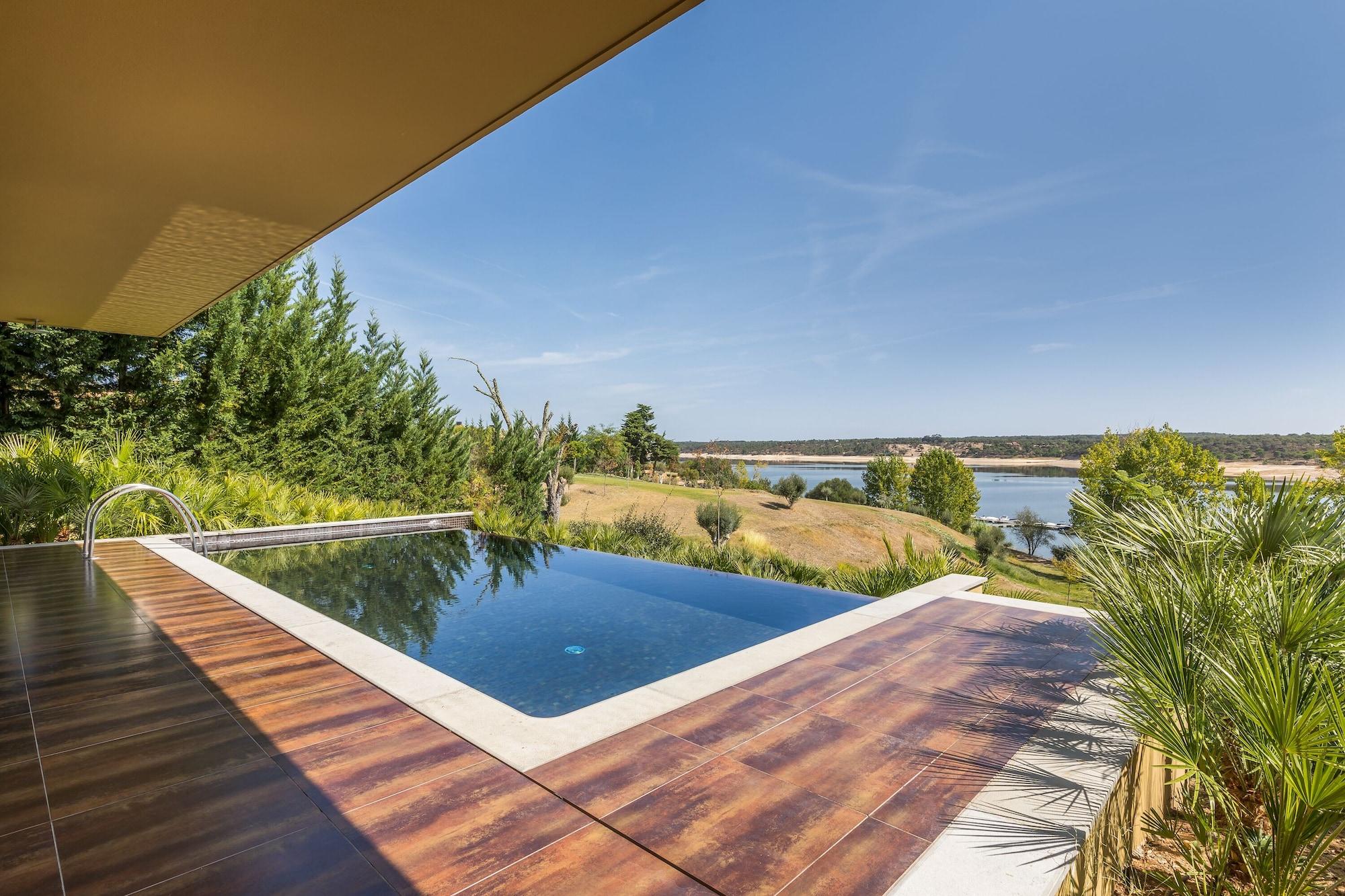 Ap Lago Montargil - Conference & Spa Luaran gambar The photo shows a luxurious infinity pool situated on a terrace or deck. The pool features a sleek, modern design with a dark blue surface that reflects the surrounding scenery. In the background, there is a landscape of rolling hills and a body of w