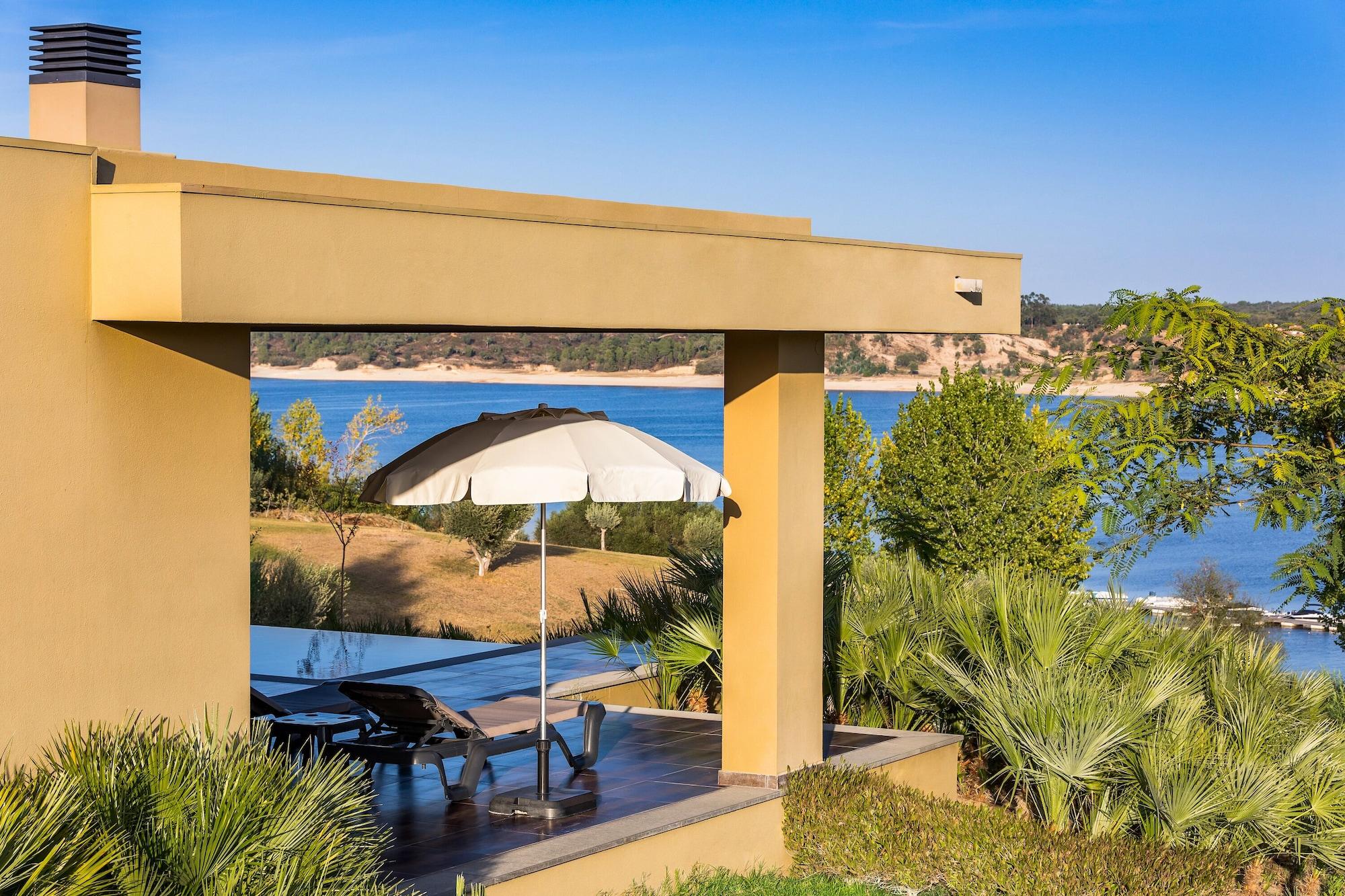 Ap Lago Montargil - Conference & Spa Luaran gambar The photo shows a peaceful outdoor area with a modern architectural structure featuring an overhang. There is a lounge chair positioned beneath a large umbrella, creating a shaded spot to relax. In the background, there is a picturesque view of a bod