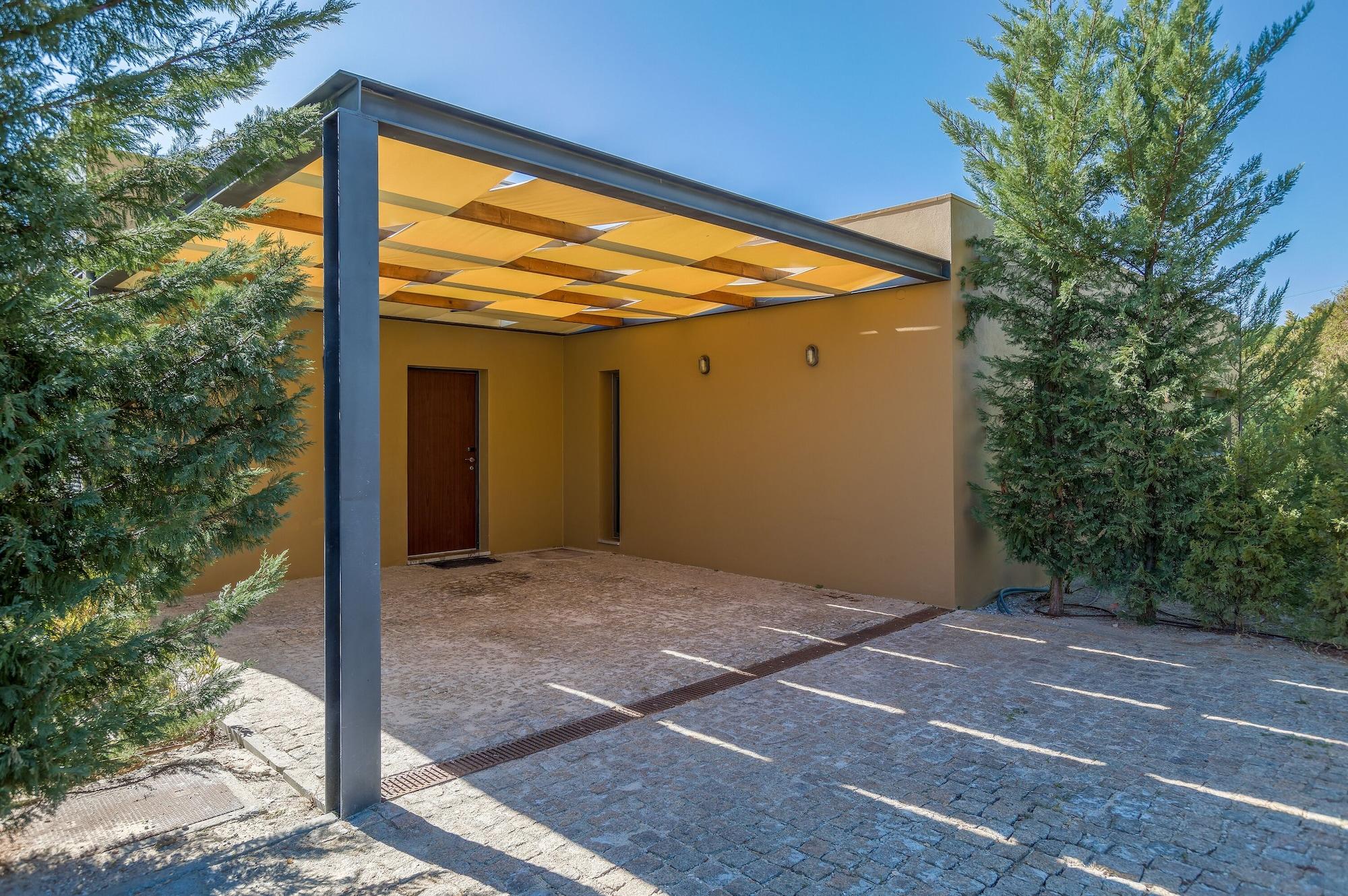 Ap Lago Montargil - Conference & Spa Luaran gambar The photo shows an exterior view of a modern structure with a carport. The carport has a sleek, metallic frame and a yellowish canopy above it. In front of the structure, there is a paved area made of stone or tiles. The main entrance features a wood