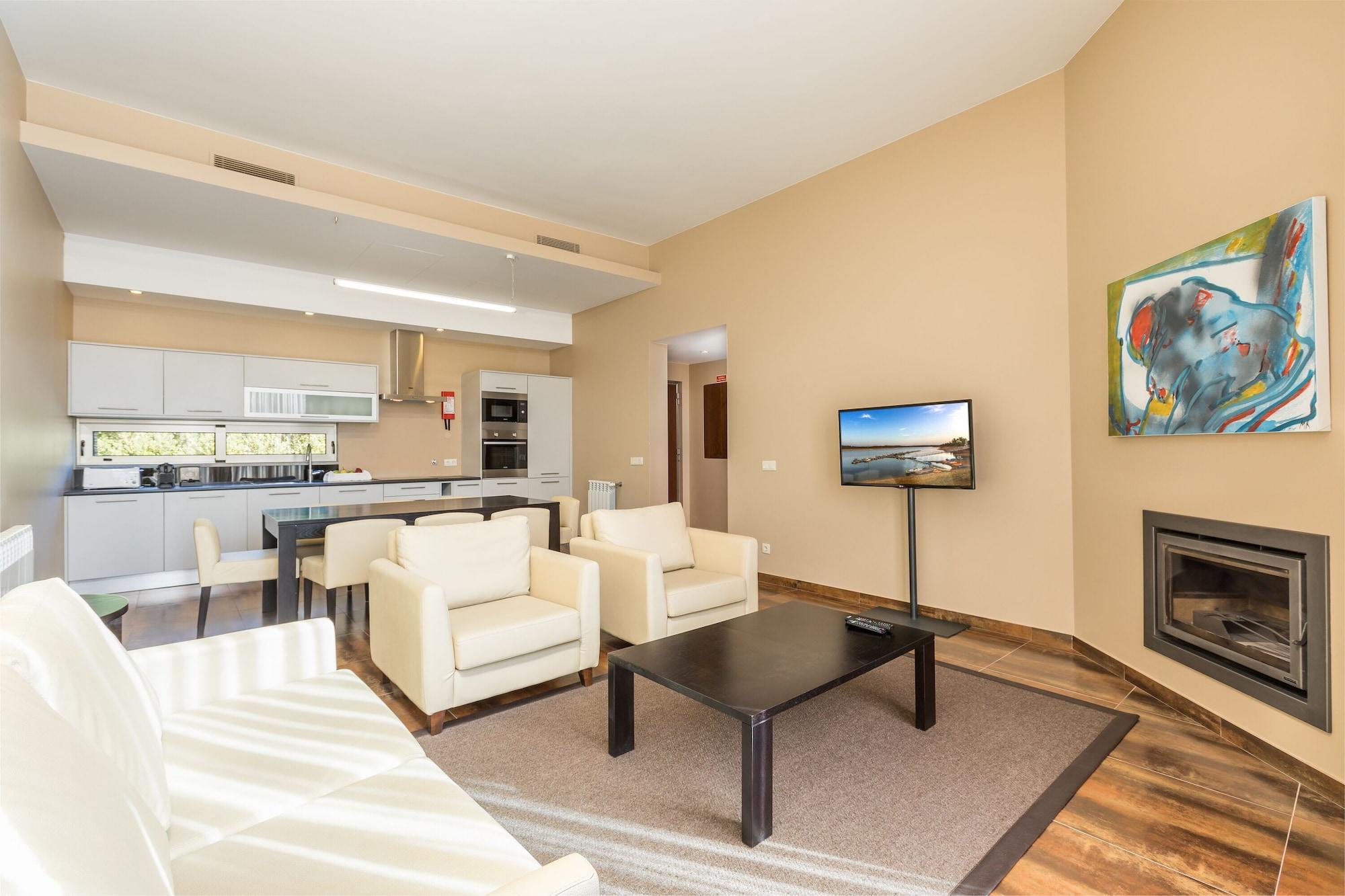 Ap Lago Montargil - Conference & Spa Luaran gambar The photo shows a modern, spacious living area with a contemporary design. The room features light-colored walls and wooden flooring. 

In the center, there is a black coffee table surrounded by four white armchairs. A flat-screen TV is mounted on th