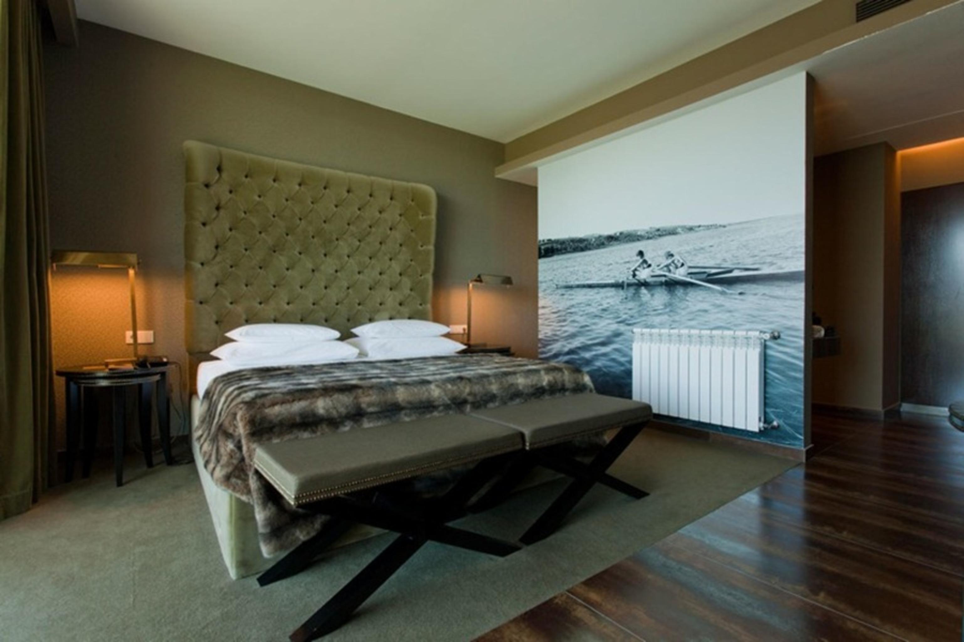 Ap Lago Montargil - Conference & Spa Luaran gambar The photo shows a modern hotel room featuring a large bed with a tufted headboard and plush bedding. The color palette is neutral, with shades of green and gray. On one side of the room, there are bedside tables with lamps. A comfortable bench sits a