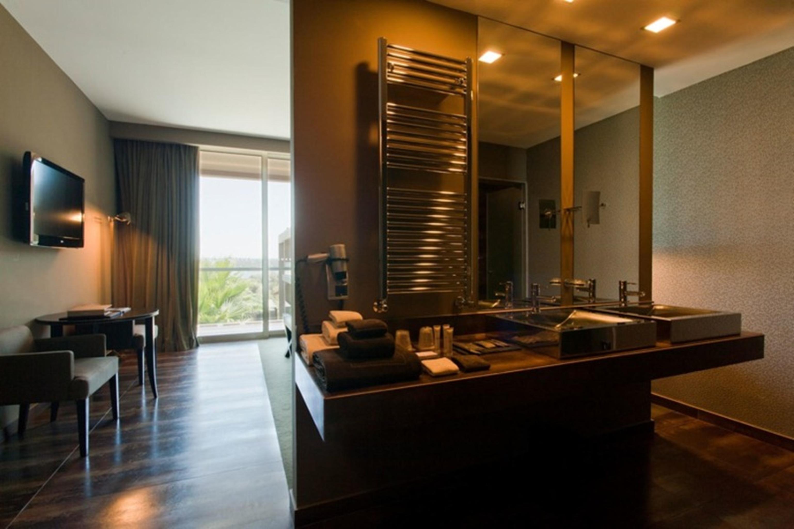 Ap Lago Montargil - Conference & Spa Luaran gambar The photo displays a modern hotel room with a contemporary design. The room features a large window, allowing natural light to enter and offering a view outside. On one side, there is a sitting area with a small table and chairs. The other side showc