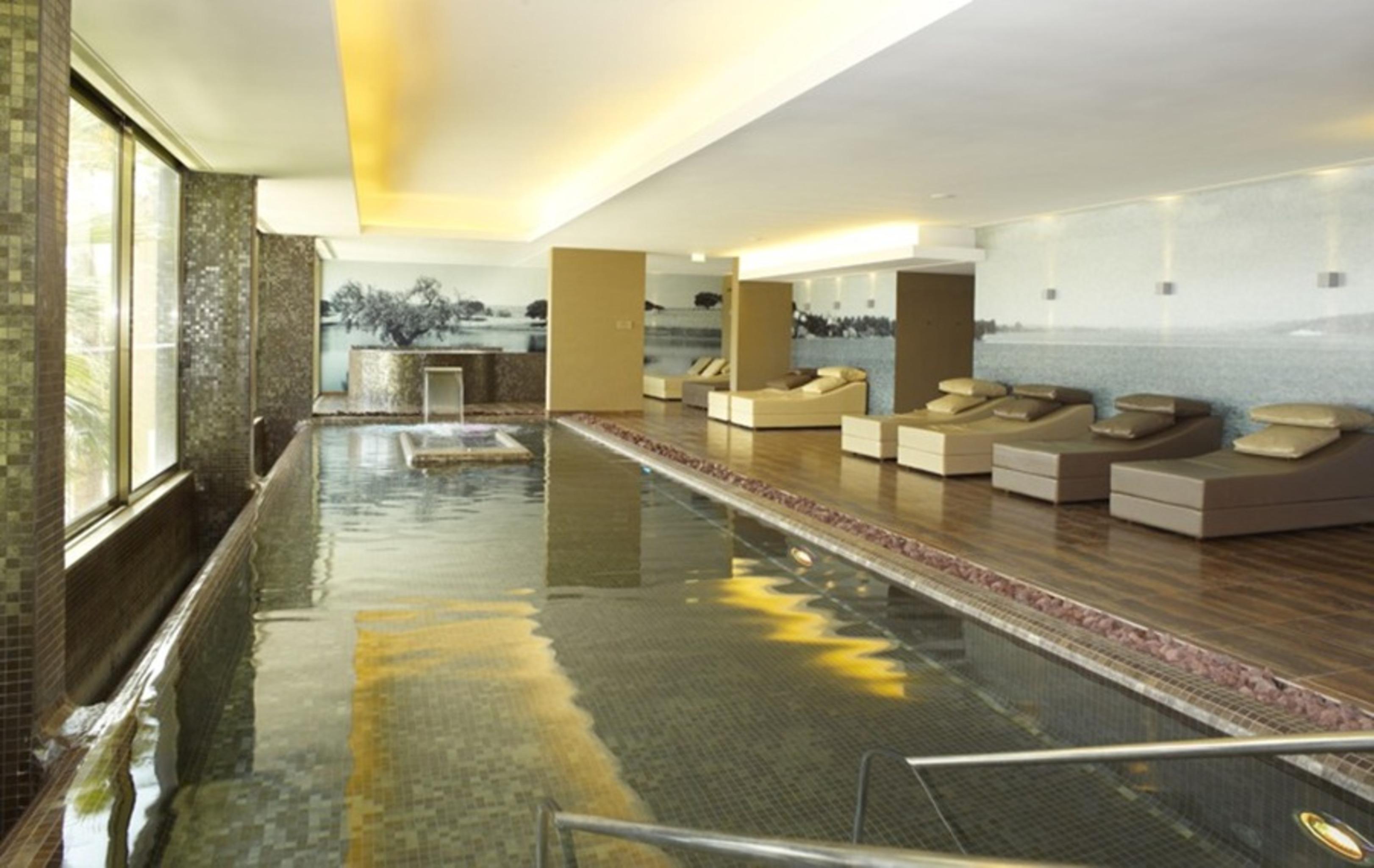 Ap Lago Montargil - Conference & Spa Luaran gambar The photo shows a modern, serene spa environment. There is a swimming pool with calm water, reflecting the surrounding decor. Along the sides, there are several comfortable lounge chairs arranged, perfect for relaxation. Large windows allow natural l