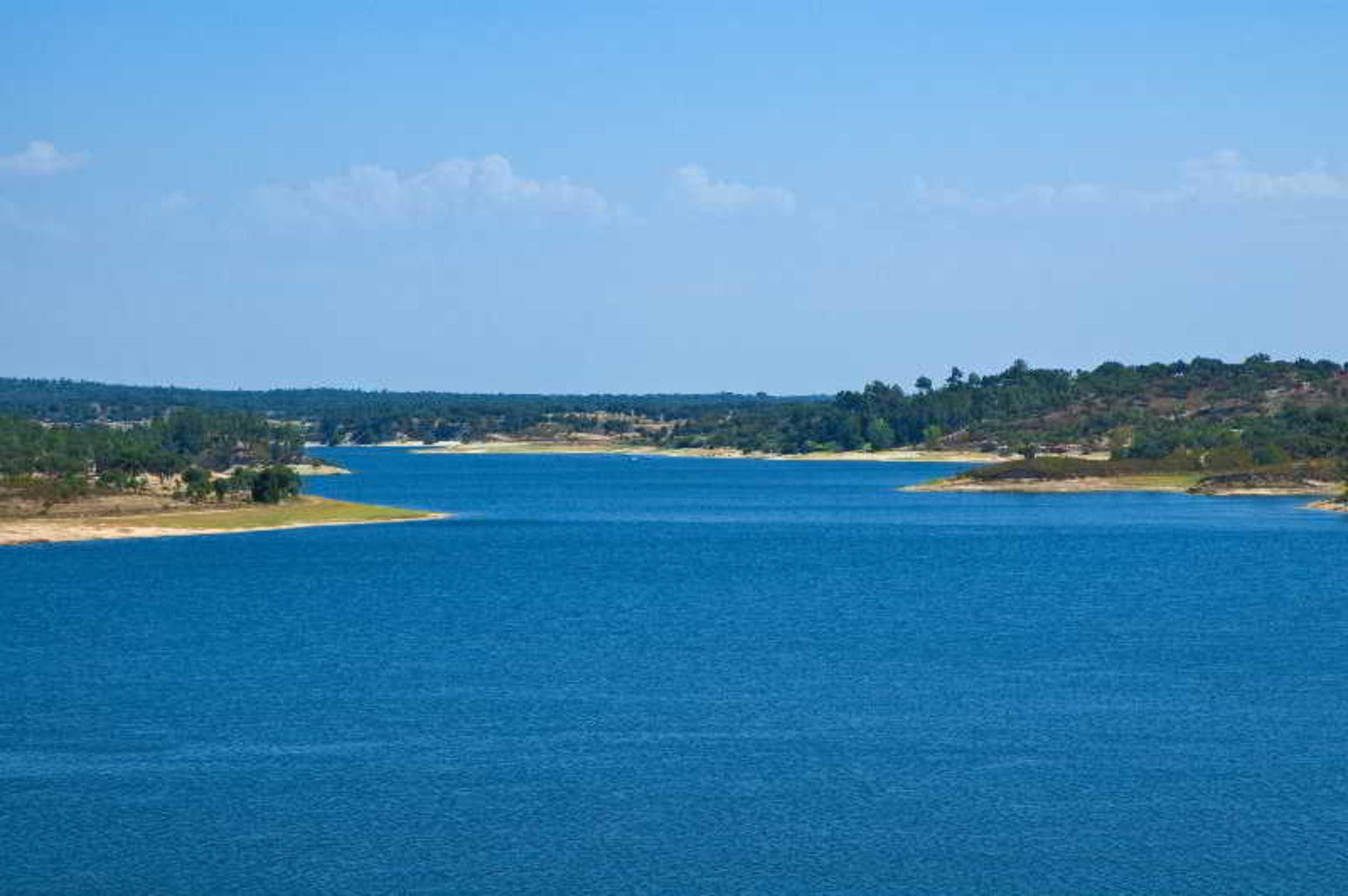 Ap Lago Montargil - Conference & Spa Luaran gambar The photo depicts a serene landscape featuring a large body of water, likely a lake or river. The water appears calm and is reflecting a clear blue sky with some clouds. Surrounding the water, there are patches of green land and trees, indicating a n
