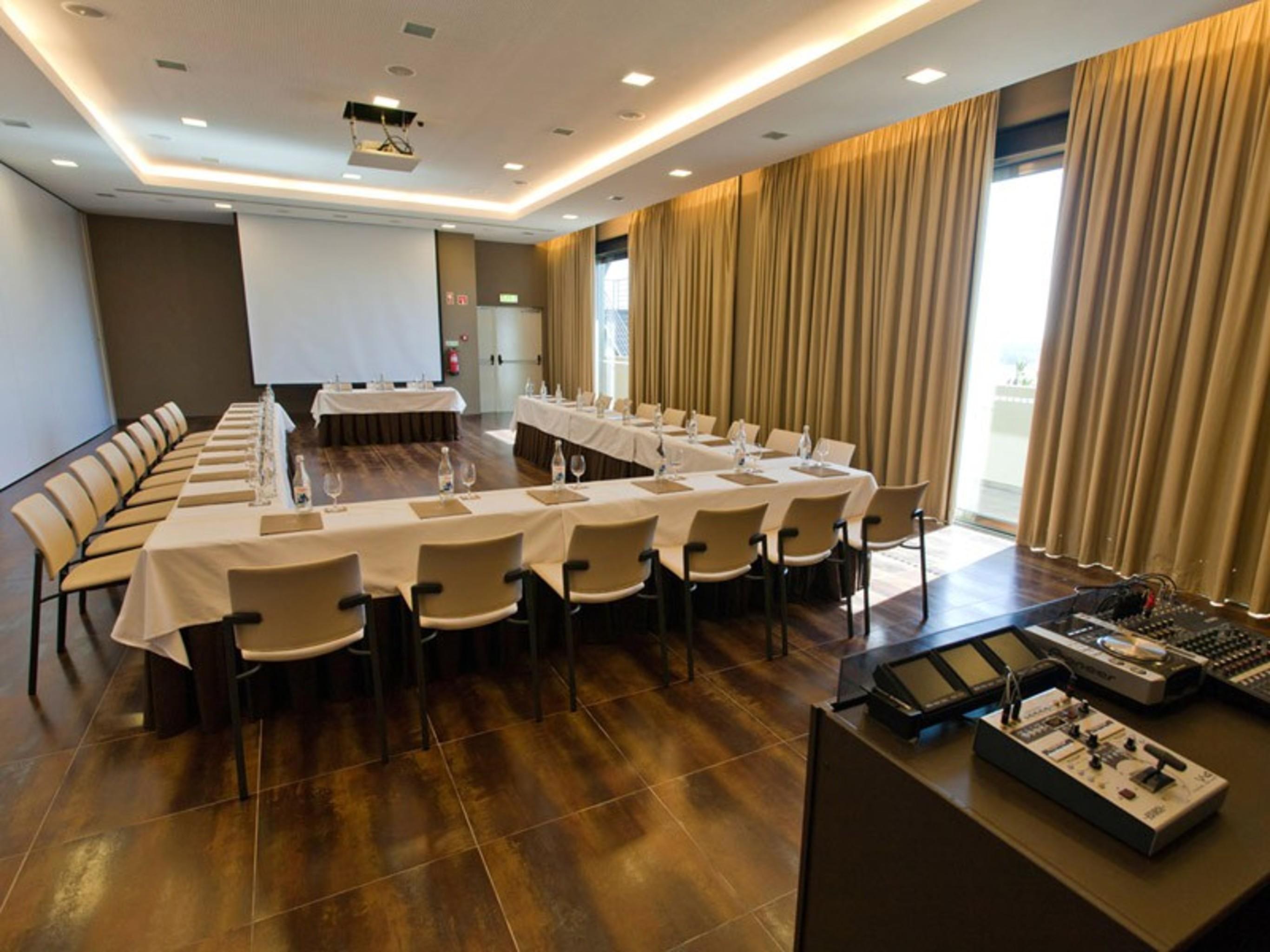 Ap Lago Montargil - Conference & Spa Luaran gambar The photo shows a modern conference room set up for a meeting. There are several tables arranged in a U-shape, surrounded by chairs. A large screen and projector are positioned at the front, with a table for speakers or presenters. The room has large