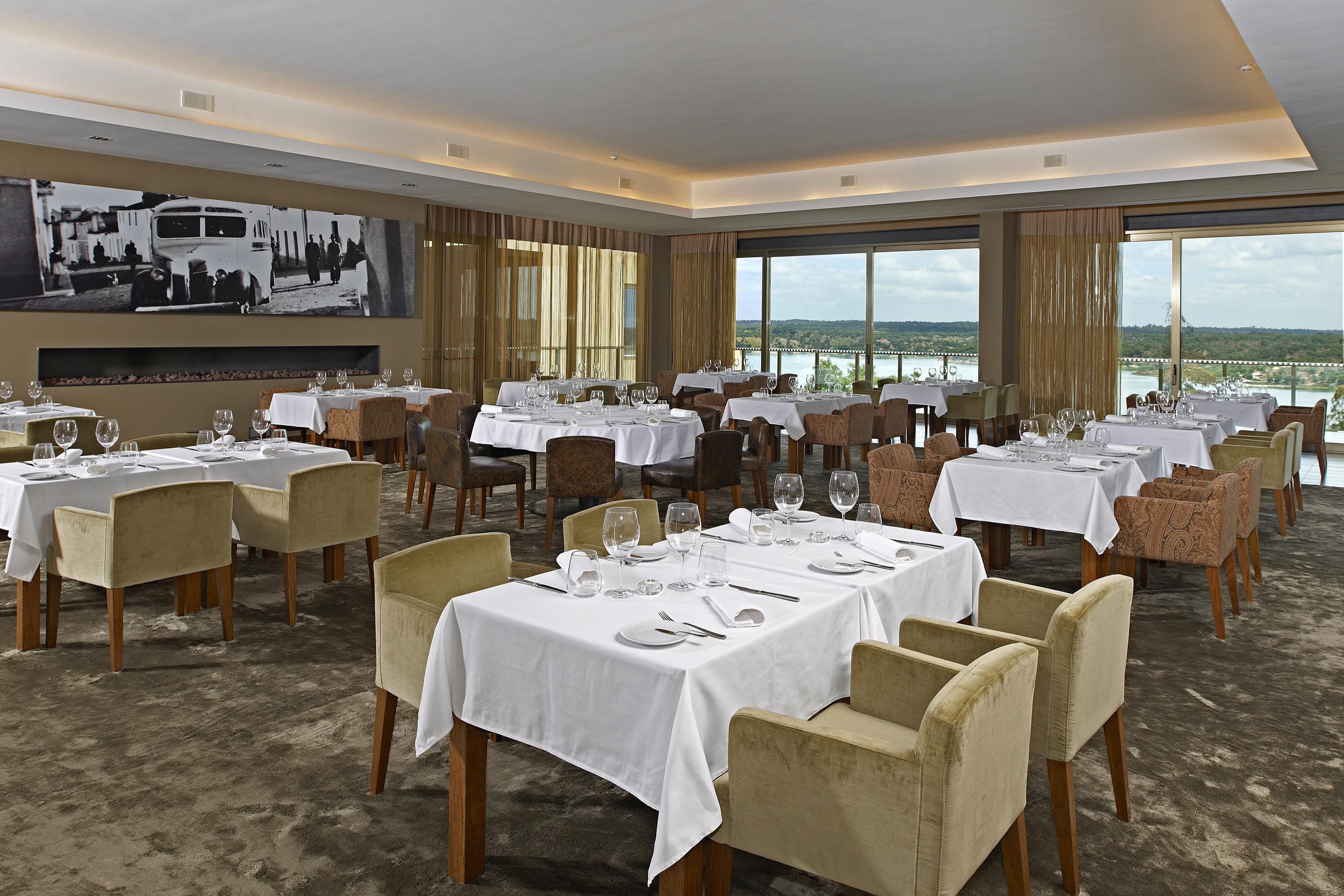 Ap Lago Montargil - Conference & Spa Luaran gambar The photo shows an elegant restaurant interior featuring neatly arranged tables with white tablecloths. Each table is set with plates, cutlery, and glasses. The seating includes a mix of upholstered chairs in different colors—some light and others da