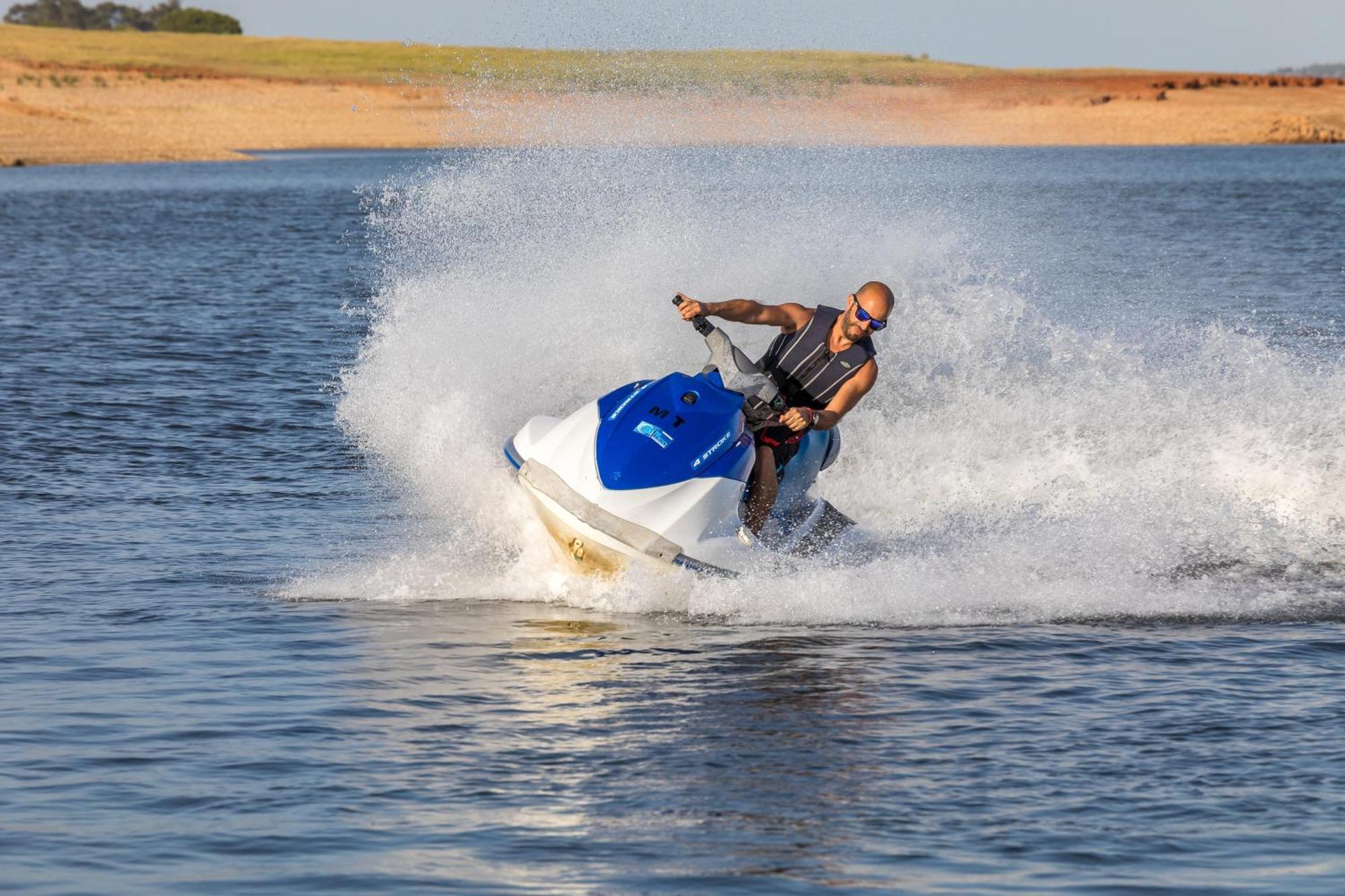 Ap Lago Montargil - Conference & Spa Luaran gambar The photo shows a person riding a jet ski over a body of water. The rider is wearing sunglasses and a life vest, leaning forward as the jet ski accelerates, creating a spray of water around them. The background features a natural landscape, likely a 