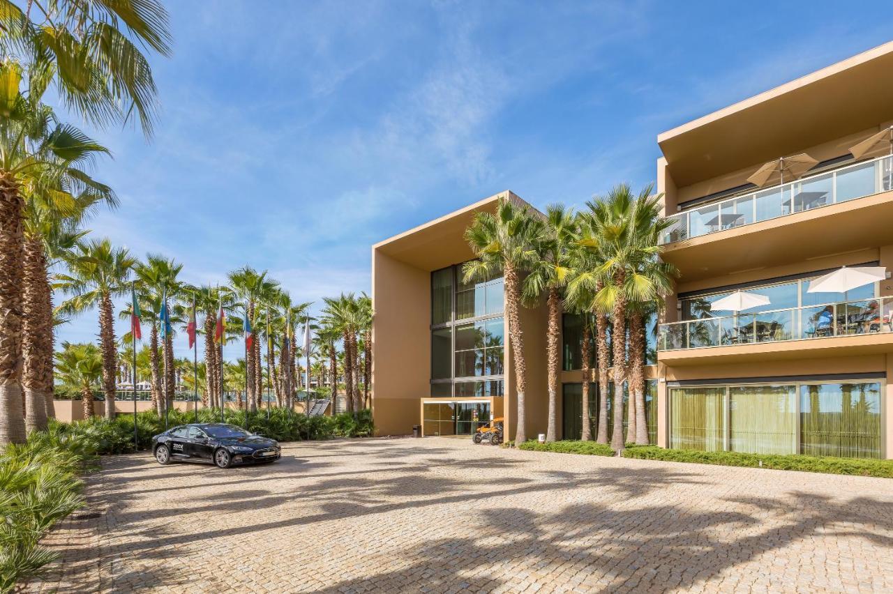 Ap Lago Montargil - Conference & Spa Luaran gambar The photo shows a modern building with a sleek design, featuring large glass windows and balconies. The structure is surrounded by a well-maintained outdoor area with palm trees, adding a tropical feel. In front of the building, there is a paved park
