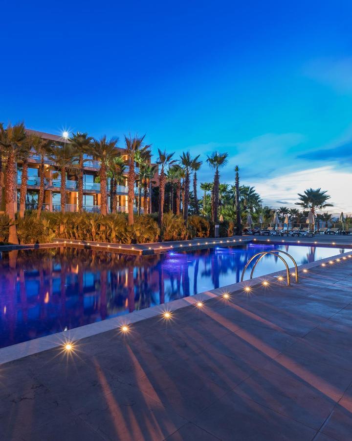 Ap Lago Montargil - Conference & Spa Luaran gambar The image shows a serene and inviting outdoor area with a large swimming pool that features a beautiful blue hue, likely illuminated by lights. Surrounding the pool are well-maintained palm trees and lush greenery, creating a tropical atmosphere. In 